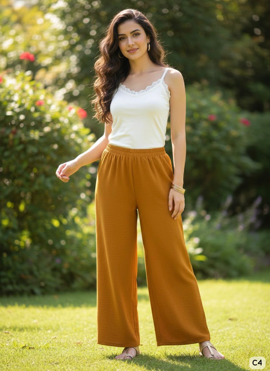 Woman wearing a white top and mustard yellow pants standing in a garden.