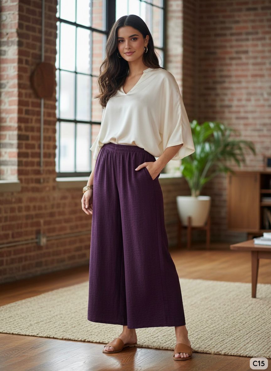 Woman wearing a white blouse and purple skirt standing in a room with brick walls and large windows.